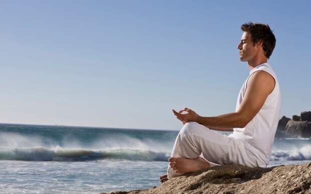 Young man meditating on rock by sea