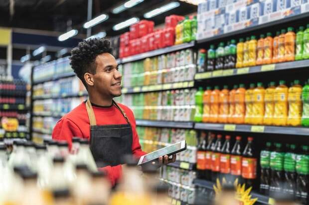 A retail store employee walking down an aisle and checking prices on a tablet.