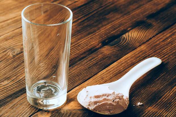 An empty glass and a spoon of protein powder on wooden table