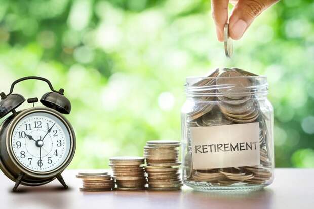 Stacks of coins on a table between a clock and a jar filled with coins with a retirement label.