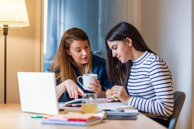 A mom chatting with her teen daughter as she works on her homework.