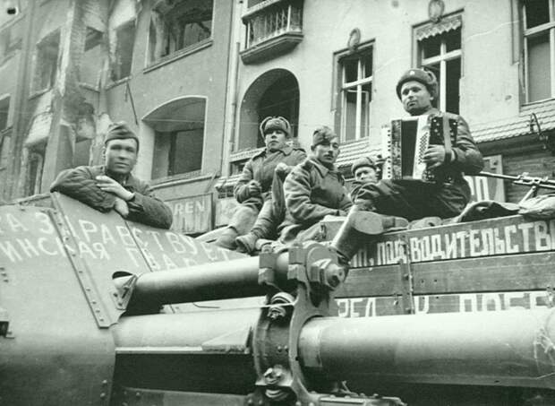 Советские артиллеристы слушают игру на аккордеоне своего товарища на улице Берлина. На переднем плане — 122-мм гаубица М-30. Артиллерия РККА, Великая Отечественная война, история