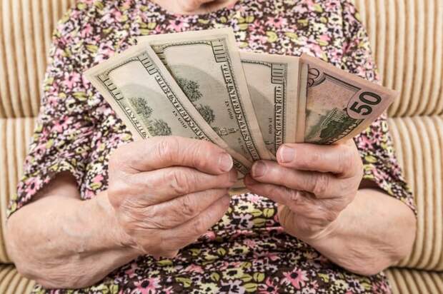 A seated person counting a fanned stack of assorted cash bills in their hands.