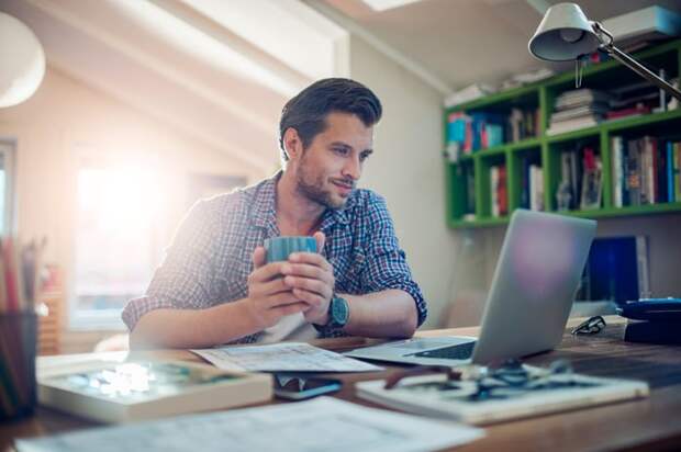 A person at a laptop holding a mug.