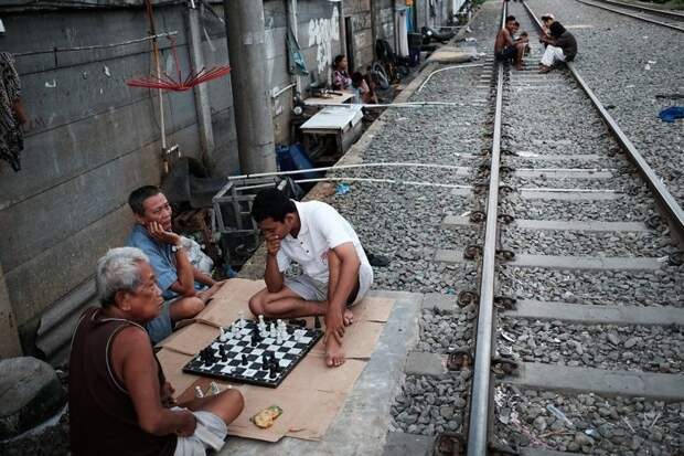 6. Мужчины играют в шахматы на земле рядом с железнодорожными путями бедность, джакарта, железная дорога, индонезия, нищета, репортаж, трущобы