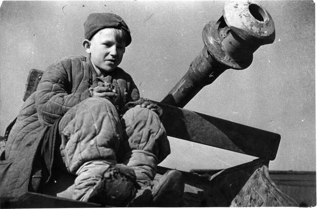 Советский подросток сидит у ствола брошенного при немецком отсуплении артиллерийского орудия.
