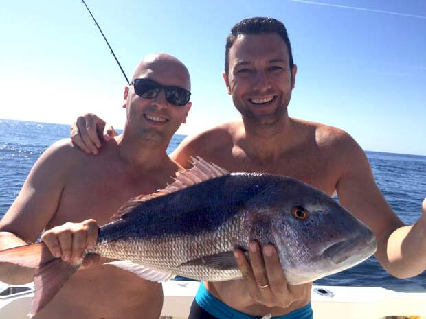 Two anglers holding a Dentex on a boat