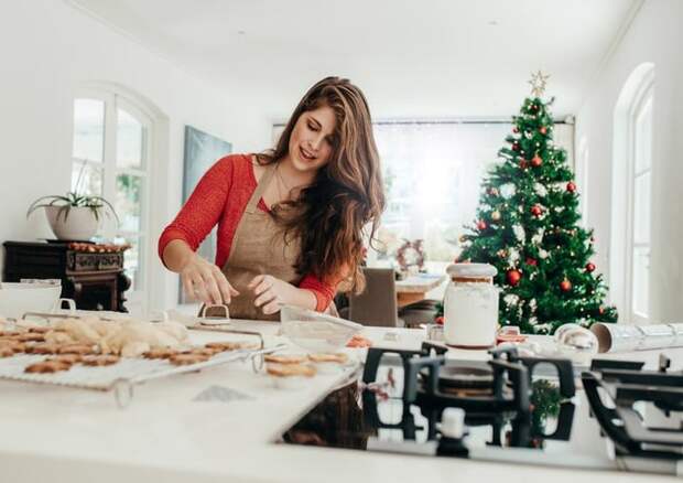 A woman baking cookies in her kitchen with a Christmas tree in the background.