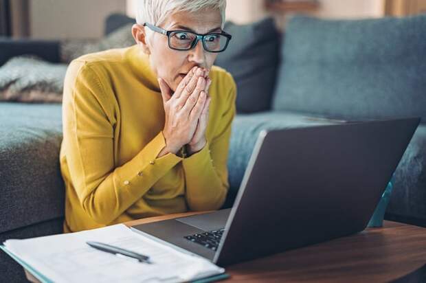 Shocked person with hands over their mouth looking at laptop.