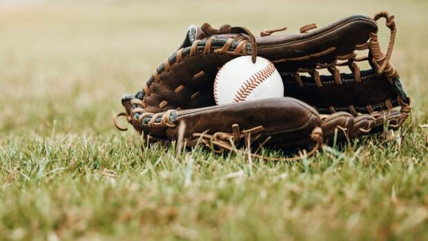 A ball and mitt sit in the outfield grass of a baseball field.