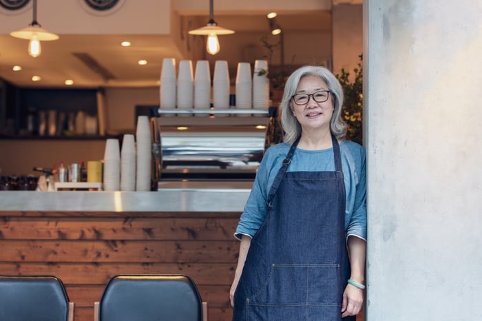 A person in an apron standing in a cafe.