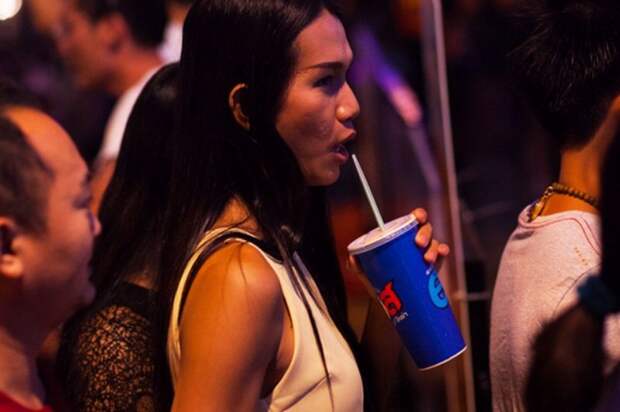 Bangkok, Thailand - December 31, 2015: A young thai transgender is standing in sidewalk in Ratchada and is drinking a Pepsi. Around are many  people. Scene is in new years night close to Ratchada and mall Street23.