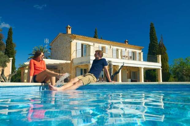 Couple lounging by an inground pool in the back yard of a large home.