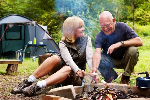 A smiling couple sitting around a campfire.