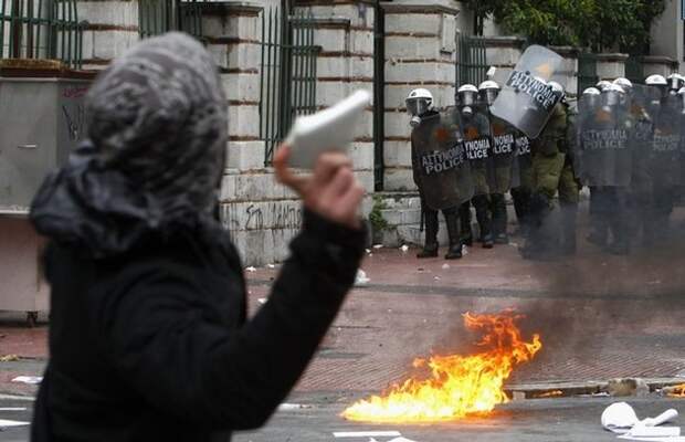 A protester throws a rock at riot policemen during a march by thousands of demonstrators in central Athens