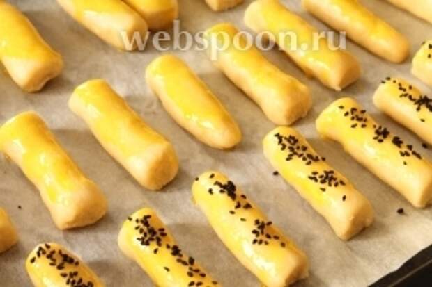 Нарезать каждую колбаску из теста на одинакового размера палочки и собрать на противень. Яичный желток, который мы отложили в сторону, взболтать слегка вилкой, добавив 2-3 столовые ложки молока или воды. Смазать им печенья и по желанию посыпать посыпкой.