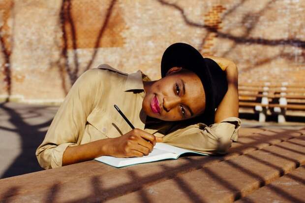 A woman sitting at a sunny park table and writing in a journal.