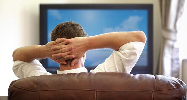 a photo of a man watching tv with his hands clasped behind his head