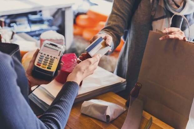 A woman holding a shopping bag and handing her credit card to the store cashier.