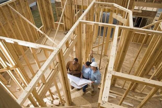 A man and woman standing in the middle of a partially constructed home looking at blueprints with their architect.