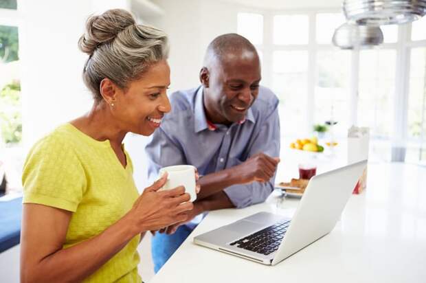 Smiling couple looking at laptop in kitchen.