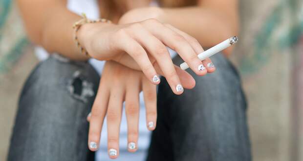 close up of a teenager's hands with sparkly nail polish and holding a lit cigarette