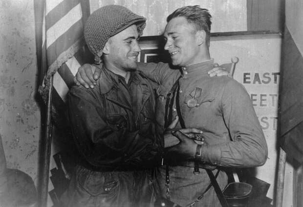 Счастливые лейтенант У. Робертсон и лейтенант А. С. Сильвашко на фоне надписи «Восток встречается с Западом», символизирующей историческую встречу союзников на Эльбе 