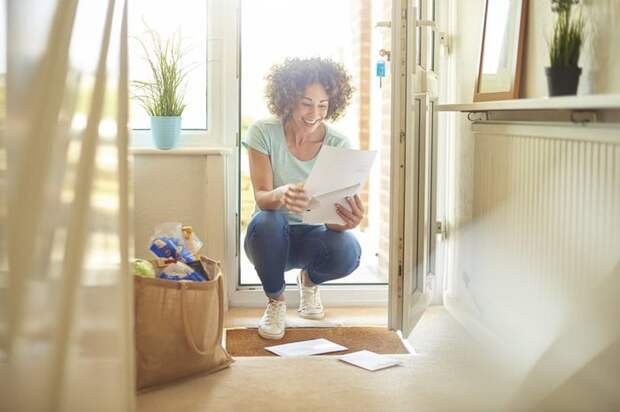 A woman smiling while opening mail in her sunny entryway.