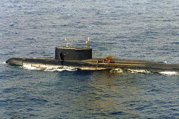 К-219 в профиль на поверхности воды. Из разрушенной ракетной шахты выбиваются оранжевые клубы оксидов азота.