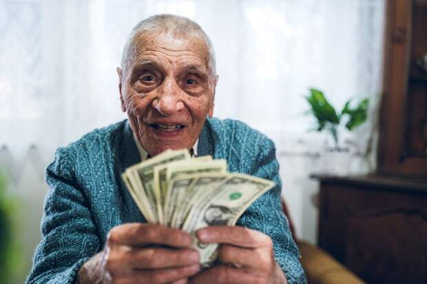 A smiling person holding a fanned assortment of cash bills in their hands.