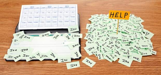 A huge pile of IOU notes with a help sign on top, sitting next to a checkbook with IOU notes on top of it.