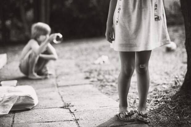 Fotografía de un niño sentado en el suelo con una niña parada
