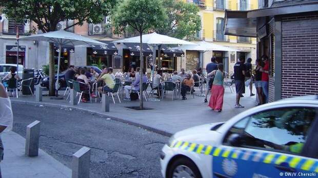 Полицейский автомобиль проезжает мимо уличного кафе в Барселоне