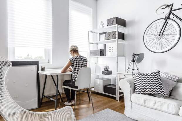 A young woman working at a small desk in the living room of her apartment.