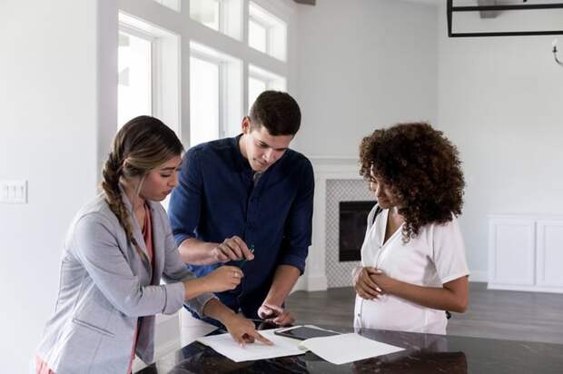 A couple standing in a new home with their realtor and signing papers.