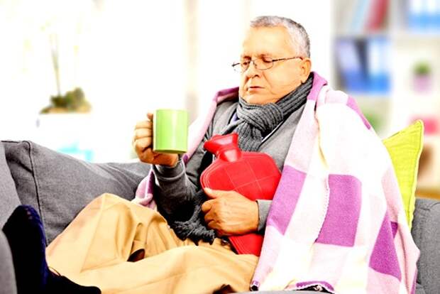 Ill man on a sofa covered with blanket drinking hot tea at home