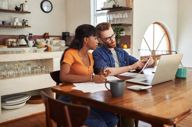 A couple reviewing bills together on a laptop while sitting in their kitchen.