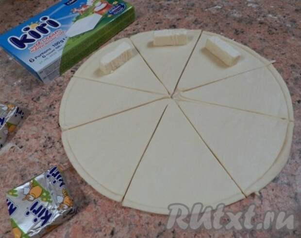 На край каждого сектора положить по 1/3 кусочка сыра Kiri, затем завернуть каждый сектор из дрожжевого слоеного теста в рогалик от края к центру. 