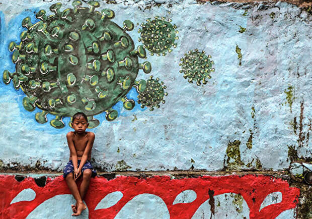 Мальчик сидит под граффити с изображением коронавируса в Богоре, Индонезия 