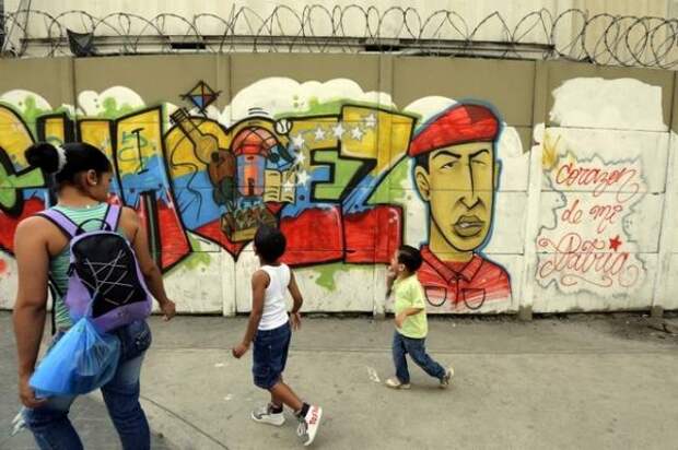 Люди проходят мимо стены с рисункомбольного президента Венесуэлы Уго Чавеса