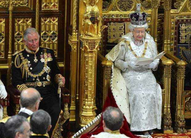 Из гардеробной королева направляется в зал заседаний палаты лордов, садится на позолоченный и украшенный государственными гербами трон. На фото: Елизавета II во время обращения к парламенту в Вестминстерском дворце (слева принц Чарльз Уэльский), 2014 год