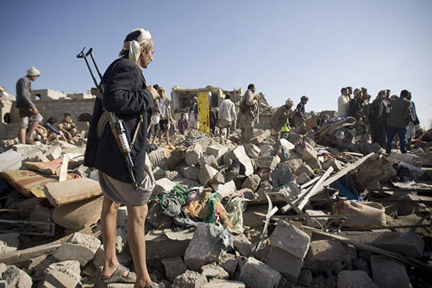 A Houthi Shiite fighter stand guard as people search for survivors under the rubble of houses destroyed by Saudi airstrikes near Sanaa Airport, Yemen, 