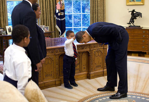 A Young Boy Reaches Up To Compare The President's Hair To His Own