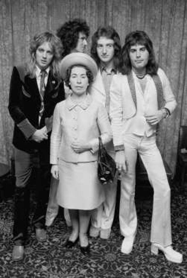 British rock band Queen posing with actress and Queen Elizabeth II look-alike, Jeannette Charles, September 1974. The group are (left to right) drummer Roger Taylor, guitarist Brian May, bassist John Deacon and singer Freddie Mercury (1946 - 1991). (Photo by Michael Putland/Getty Images)