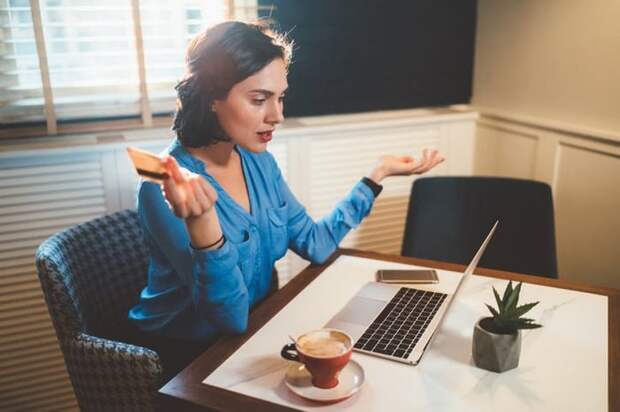 A woman looking frustrated with a credit card in her hand while looking at a laptop.