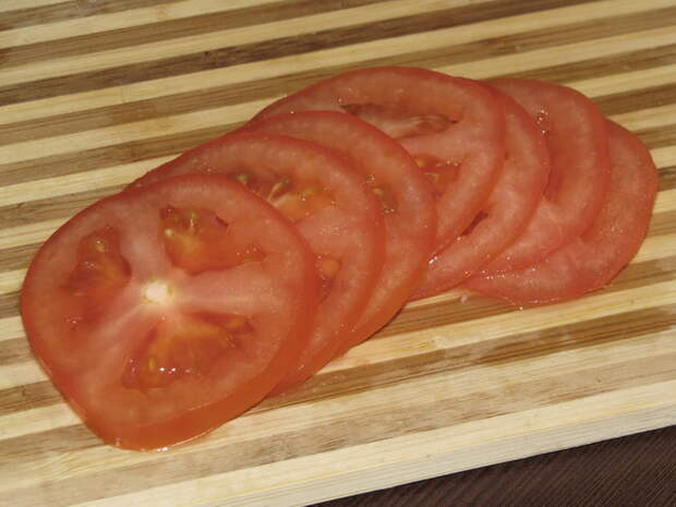 Помыть помидор и нарезать его тонкими кругляшками. пошаговое фото этапа приготовления слоеного салата Радуга