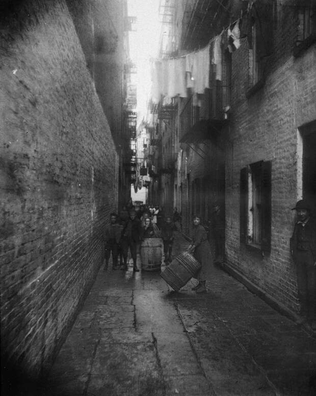 circa 1890: Children play with barrels in an alley between tenement buildings in Gotham Court, 38 Cherry Street, New York City. (Photo by Jacob A. Riis/Museum of the City of New York/Getty Images)