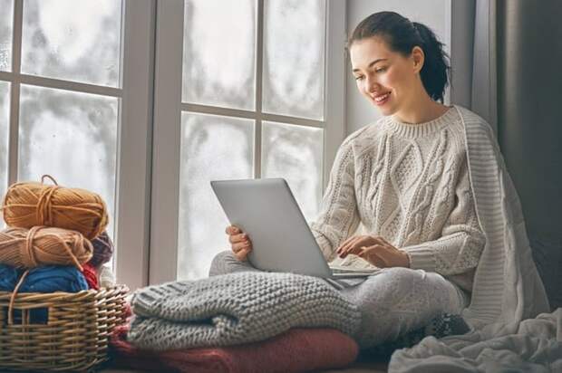 A woman working on her laptop by a window in her home.