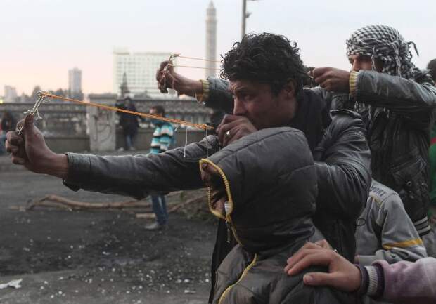 Protesters use slingshots to launch stones at riot police during clashes near Qasr el-Nil bridge, in Cairo