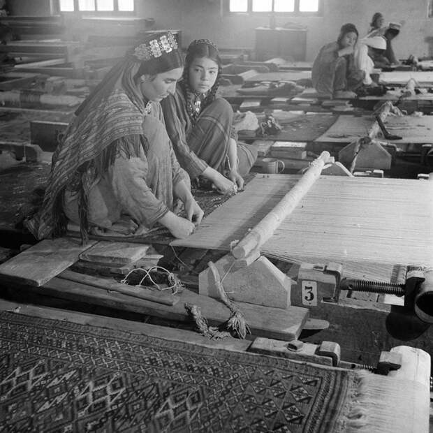 Девушки ткут полотна на ткацких станках.